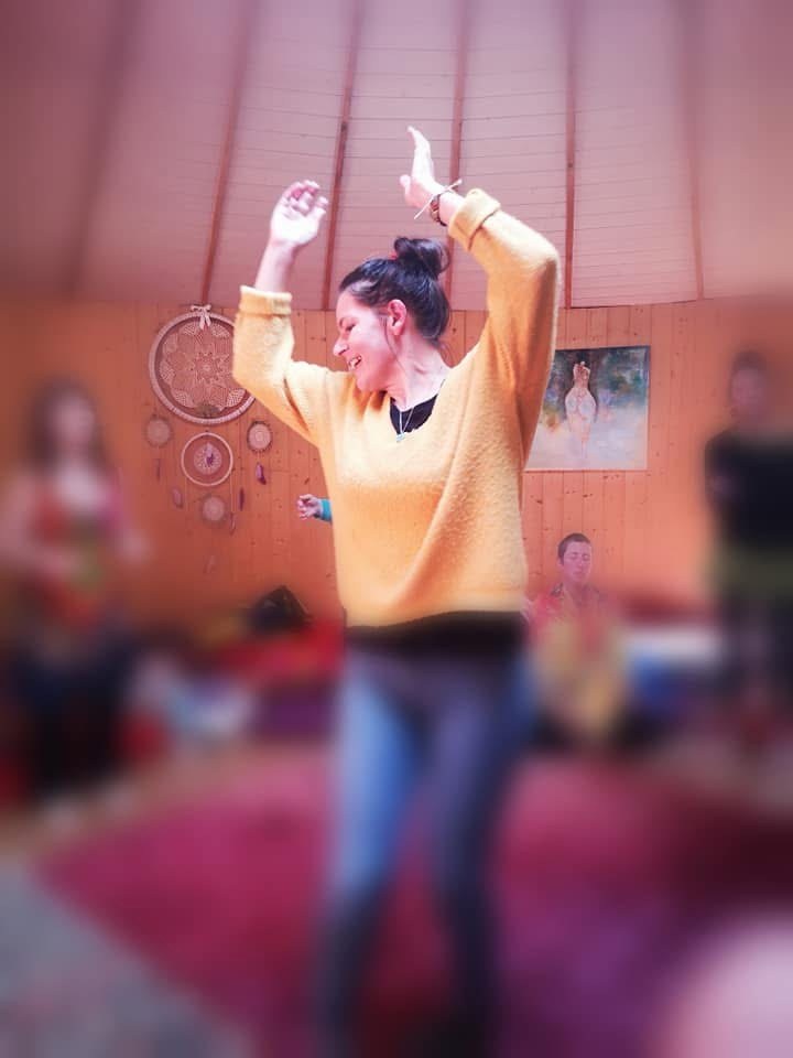 Une femme en pull jaune danse, les bras levés, pendant un atelier